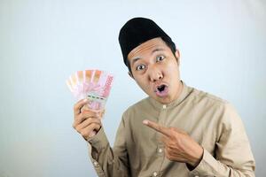 gracioso facial expresión conmocionado y sorpresa asiático musulmán hombres vistiendo gorra mientras participación dinero foto