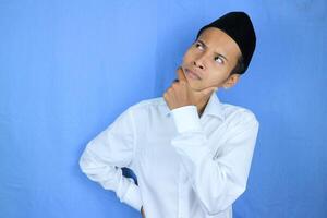 Confuse expression of asian muslim man doing thinking gesture, looking for idea on white background photo