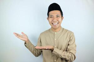 Smiling expression of muslim asian man, presenting and showing an empty space. Advertising concept photo