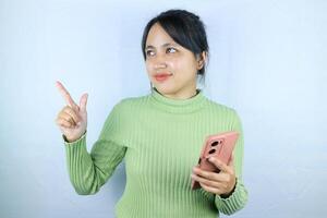 Smiling asian woman holding smart phone while pointing finger on white background photo