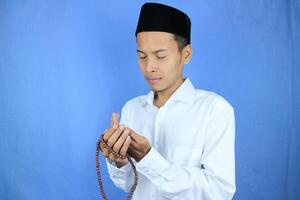 Muslim asian man holding prayer beads on blue background. Ramadan kareem and ied mubarak concept. photo