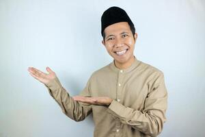 Smiling expression of muslim asian man, presenting and showing an empty space. Advertising concept photo