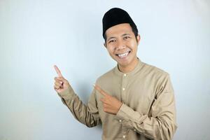 Smiling expression of muslim asian man, pointing finger an empty space. Advertising concept photo