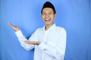 Smiling expression of muslim asian man, presenting and showing an empty space. Advertising concept photo