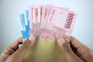 female hands holding open craft paper envelope with one hundred thousand rupiah banknotes photo