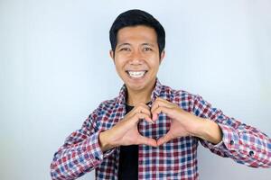 Young asian man isolated on white background smiling and gesturing a heart shape with hands photo