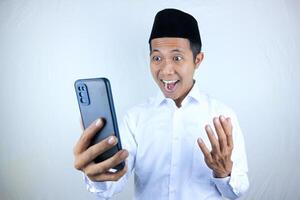 Muslim asian man showing excited expression while holding mobile phone reading message photo