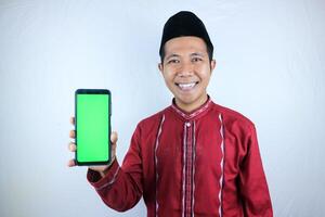 Smiling happy of muslim asian man wearing cap showing empty phone screen. Advertising concept photo