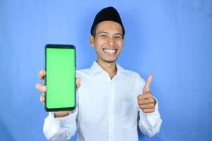 Smiling happy of muslim asian man wearing cap showing empty phone screen. Advertising concept photo