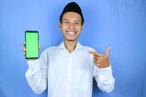 Smiling happy of muslim asian man wearing cap showing empty phone screen. Advertising concept photo