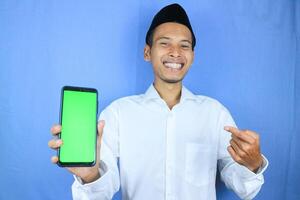 Smiling happy of muslim asian man wearing cap showing empty phone screen. Advertising concept photo