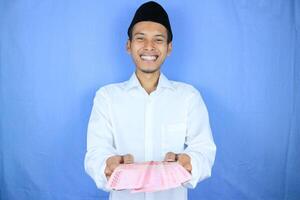 Smiling expression of Asian Muslim man giving money for helping, donation or zakat photo