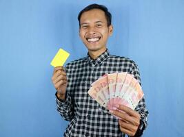 Excited expression handsome asian man hold empty card and money banknotes. Finance concept. photo