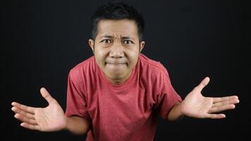 Asian man in red tshirt showed no idea gesture, shrugged and raised his hand. isolated on black photo