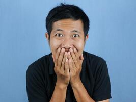 Shocked and surprised face of Asian man Covering mouth with hands in isolated on blue background. photo