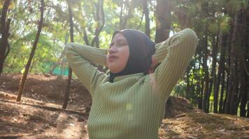 muslim woman with hands behind head and eyes closed breathing fresh air in middle of pinewood forest photo