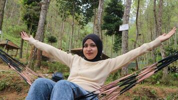 Young woman with headscarf resting in comfortable hammock at green garden photo