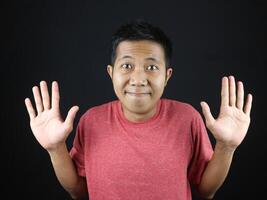 Asian man in red tshirt showed no idea gesture, shrugged and raised his hand. isolated on black photo