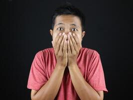 Young excited Asian man with hand covering mouth isolated on black studio background with copy space photo