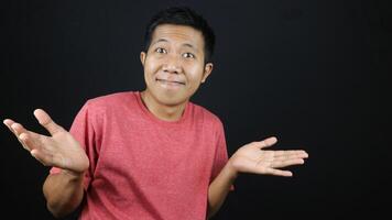 Asian man in red tshirt showed no idea gesture, shrugged and raised his hand. isolated on black photo