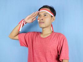 Serious expression indonesian man wearing red and white headband posing to salute indonesian flag photo