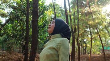 Happiness concept. Arab Woman eyes closed and breathing fresh air at pine forest with sunlight. photo