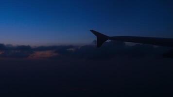 visie van een vliegtuig vleugel tegen een bewolkt nacht lucht. patrijspoort, avond vlucht video