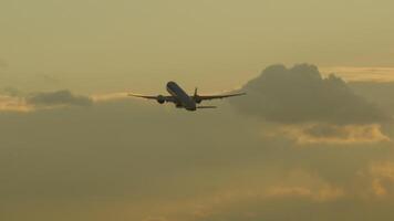 Jet civilian aircraft with unrecognizable livery climbing after takeoff in the sunset cloudy sky, long shot, rear view. Cinematic footage of an airliner flying high in the sky video