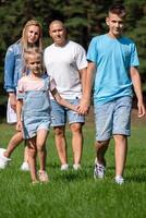 A family of four walks hand in hand through a sunny park, showcasing a moment of unity, bonding and peaceful coexistence, used for National Siblings day and brother sister themes. photo