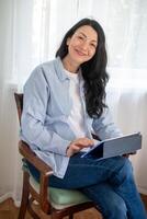 Mature woman in cozy attire, is using tablet, reading something, and smiling showcasing ease with technology during midlife transition, and lifelong learning photo