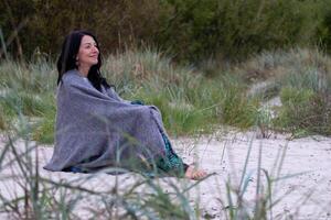 A contemplative woman nestles in a soft shawl outdoors, her smile reflecting an inner peace, hinting at the grace of aging and the calm of emotional maturity. photo