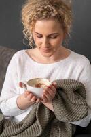 A relaxed woman in a cozy sweater enjoys the aroma of her coffee, creating a sense of comfort and a peaceful break in a homely setting. photo