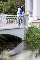 A woman leans on a white balustrade by a pond, amid nature, reflecting serenity and contemplation, suggesting themes of midlife and tranquility. photo