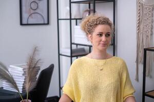 A woman in a yellow top with a thoughtful expression sits in an office, suggesting a moment of reflection or planning amidst a professional setting. photo