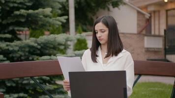 vrouw maken vergelijking van papieren en laptop versie van het buiten kantoor. video