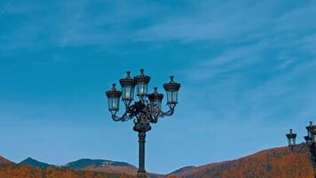 Two black street lamps of old style. Low angle view. Mountains in sunny autumn daytime at backdrop. video