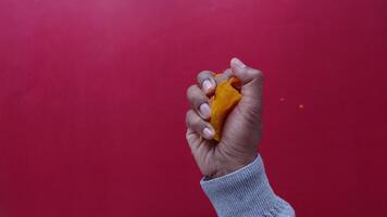 A closeup view capturing a hand squeezing a crispy snack against a vibrant red background video