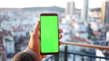 mano de hombre joven usando un teléfono inteligente con pantalla verde contra edificios de la ciudad video