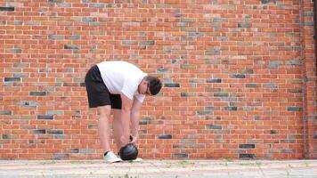 sports and leisure. strong Caucasian man working out using kettlebell in the park, brick wall background video