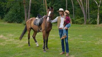 cowboy e il suo figlia con un' cavallo su il prato. contento cowboy famiglia. lento movimento. video