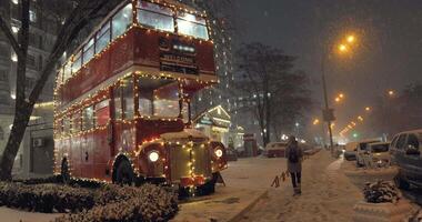 Heavy snowfall on Christmas evening against the backdrop of a red bus double decker. 4K video