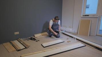 A builder in a work overalls is assembling a bed. Assembling furniture in a new apartment. video