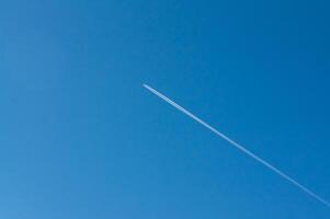 Against the serene blue sky, a jet streaks, its contrail a fleeting mark of human passage, connecting distant places and leaving a temporary imprint on the vastness of the atmosphere. photo