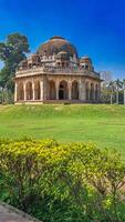 Ancient Tomb of Muhammad Shah Sayyid in Lodhi Garden in New Delhi. The tomb is architectural marvel with a large dome and intricate carvings on facade. lush green grass and vibrant yellow-green shrubs photo