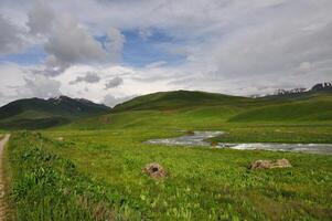 Mountain river, hills, meadows and gravel path. Adventure travel to Kyrgyzstan mountains. Outdoor, trekking, camping. Hiking, valley floor. Solitude, recreation. Mountain tourism, alpine scenery photo