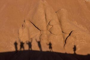 The elongated shadows of tourists traverse the undulating canyon walls, a stark contrast of human vivacity against the still, enduring formations sculpted by the relentless forces of nature over time. photo
