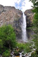 Waterfall from the mountain, Kyrgyzstan. Hiking trail, valley floor. Adventure travel to backcountry. Solitude, recreation. Outdoor, trekking. Tourism with camping backpack and alpine scenery photo