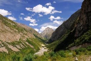Adventure travel to Kyrgyzstan mountains. Hiking trail, valley floor, gravel path. Mountain tourism, towering cliffs, alpine scenery. Solitude, recreation. Outdoor exploration, trekking camping photo
