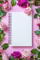 Spiral Notebook Surrounded by Pink Roses on Pink Background photo