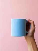 Hand Holding Blue Coffee Mug on Pink Background photo